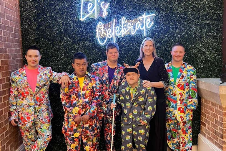Photo: Pinkerton Boys Adventures/Facebook Photo shows a mother with six young men who have Down syndrome wearing colorful suits.