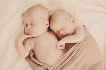Image shows two babies snuggled in a tan blanket.