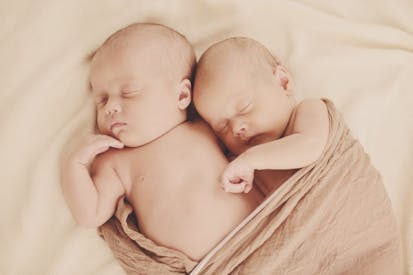 Image shows two babies snuggled in a tan blanket.