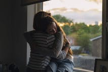 Photo: Justin Paget/Getty Images Powerful view of a young teenage girl being comforted by her mother as she sits on her window sill at sunset