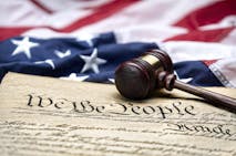 American flag draped around a judge's gavel block and the United States Constitution for use as a symbol of laws, freedom and separation of government powers.