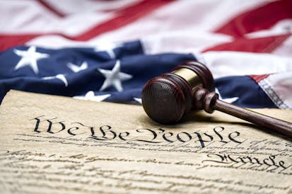 American flag draped around a judge's gavel block and the United States Constitution for use as a symbol of laws, freedom and separation of government powers.