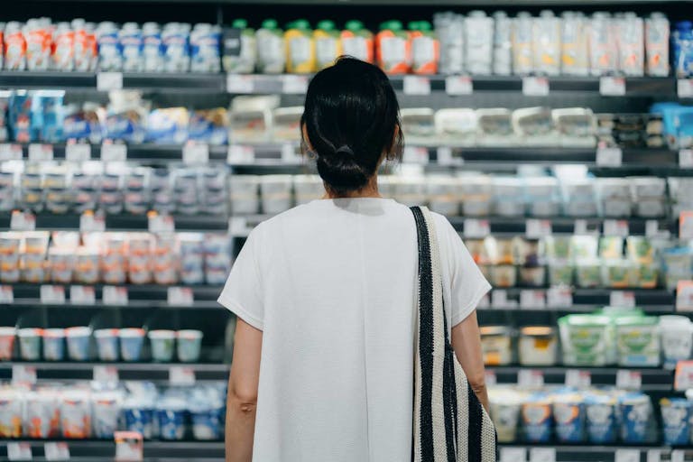 Photo: d3sign/Getty Images Rear view of young Asian woman doing grocery shopping, standing in front of a shelf full of fresh dairy products in the dairy aisle and thinking which product to choose from in a supermarket. Concept of customer awareness