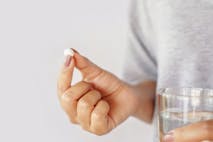 Photo shoes a woman holding a pill and a glass of water.