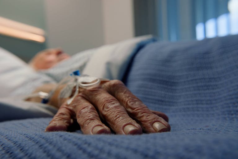 Elderly man, hands and bed in hospital for with iv drip for stroke, healthcare and medicine. Senior patient, sleeping and gurney in clinic for cancer, health and life extension drugs with metmorfin