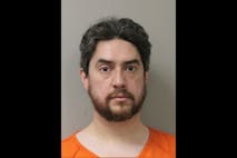 Image shows a bearded man in an orange jumpsuit posing for a mugshot.