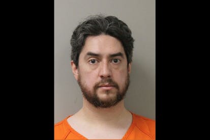 Image shows a bearded man in an orange jumpsuit posing for a mugshot.