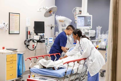 A female doctor and a male nurse are busy hooking up monitoring equipment and preparing the unrecognizable injured woman for the examination in the emergency room.