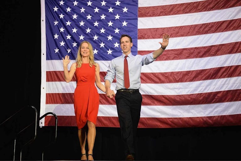 Image shows Erin Hawley and Sen. Josh Hawley walking on stage in front of an American flag.