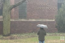 Photo: MLive Image shows a pro-life activist standing in the rain in front of the brick building housing Grand Rapids Planned Parenthood.