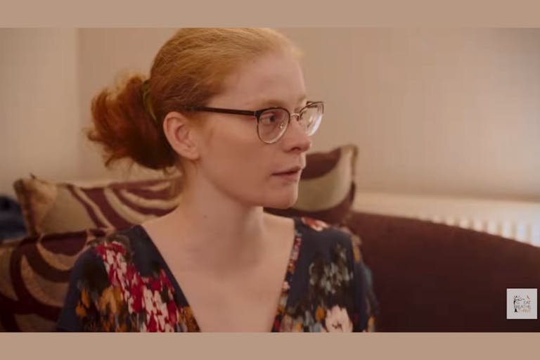 Photo: Screenshot Eat Breathe Thrive Foundation for Eating Disorders Ailidh wears glasses and her red hair in a bun while sitting on a maroon couch.