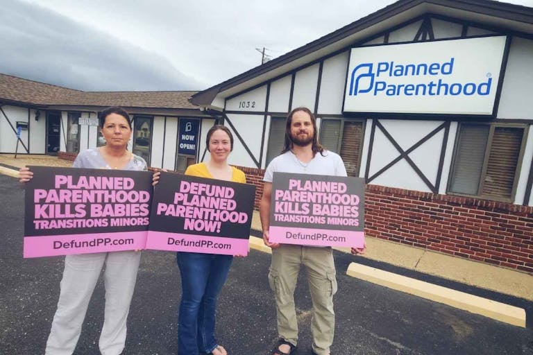Image shows three pro-life activists holding Defund Planned Parenthood signs outside of the now-closed Rolla Planned Parenthood in 2025.