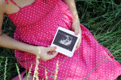 A pregnant teen wearing a pink polka dot dress while holding an ultrasound photo.