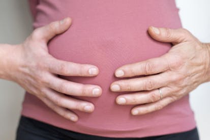 Two hands on the belly of a pregnant woman wearing a pink shirt.