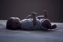 Photo: Martins Rudzitis/Getty Images baby laying on white surface with face turned away from the camera