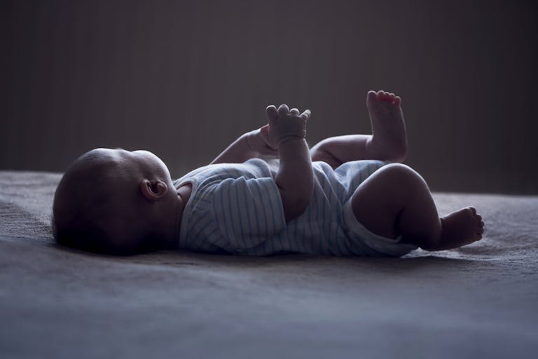 Photo: Martins Rudzitis/Getty Images baby laying on white surface with face turned away from the camera