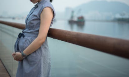 7 months pregnant women standing against a balustrade in a waterfront park along Victoria Harbour.