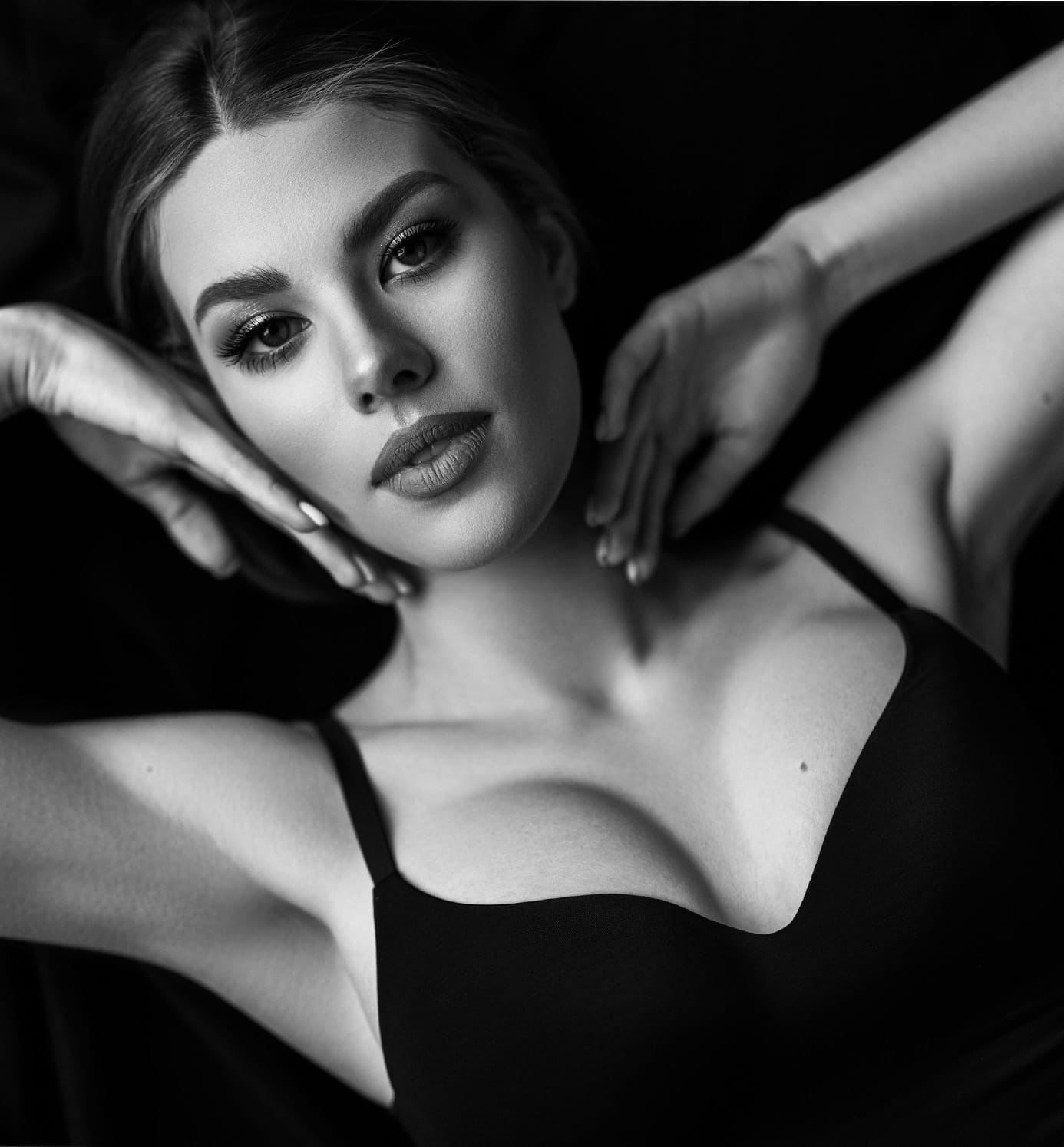greyscale of woman laying down with hands on face in black bra