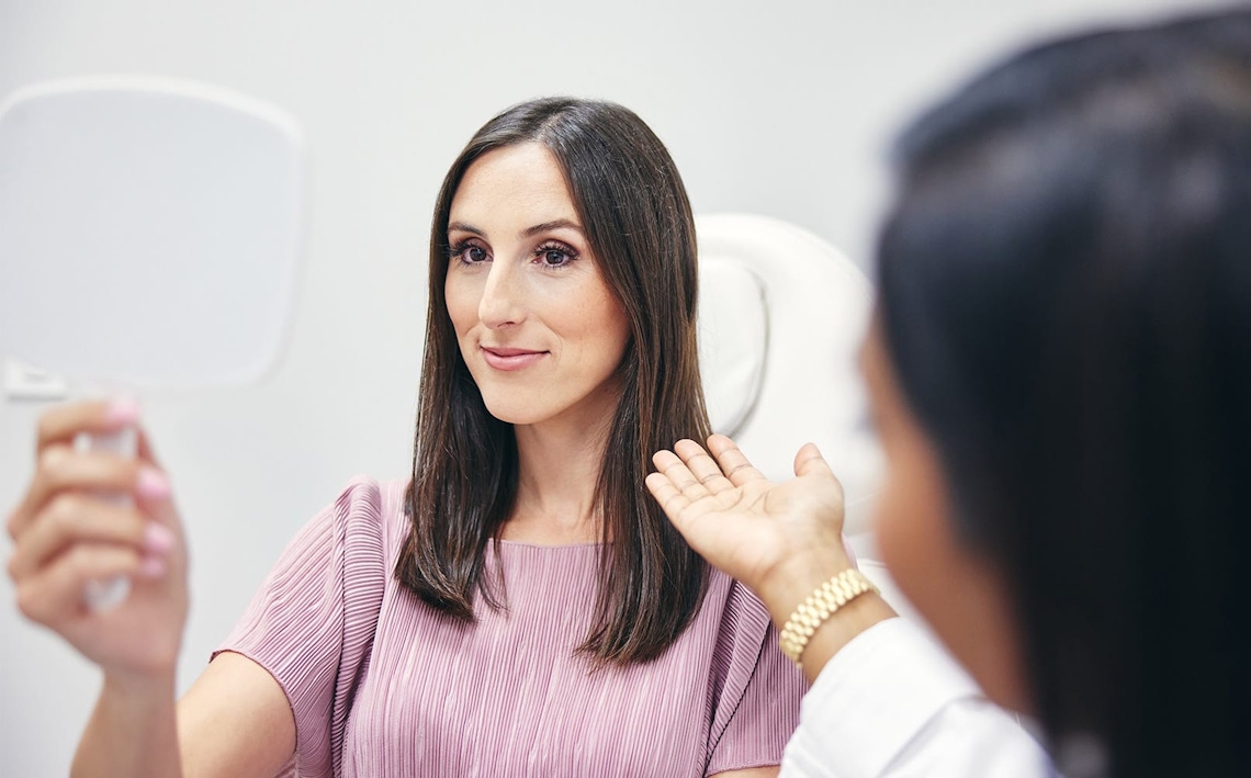 woman with brown hair looking into handheld mirror