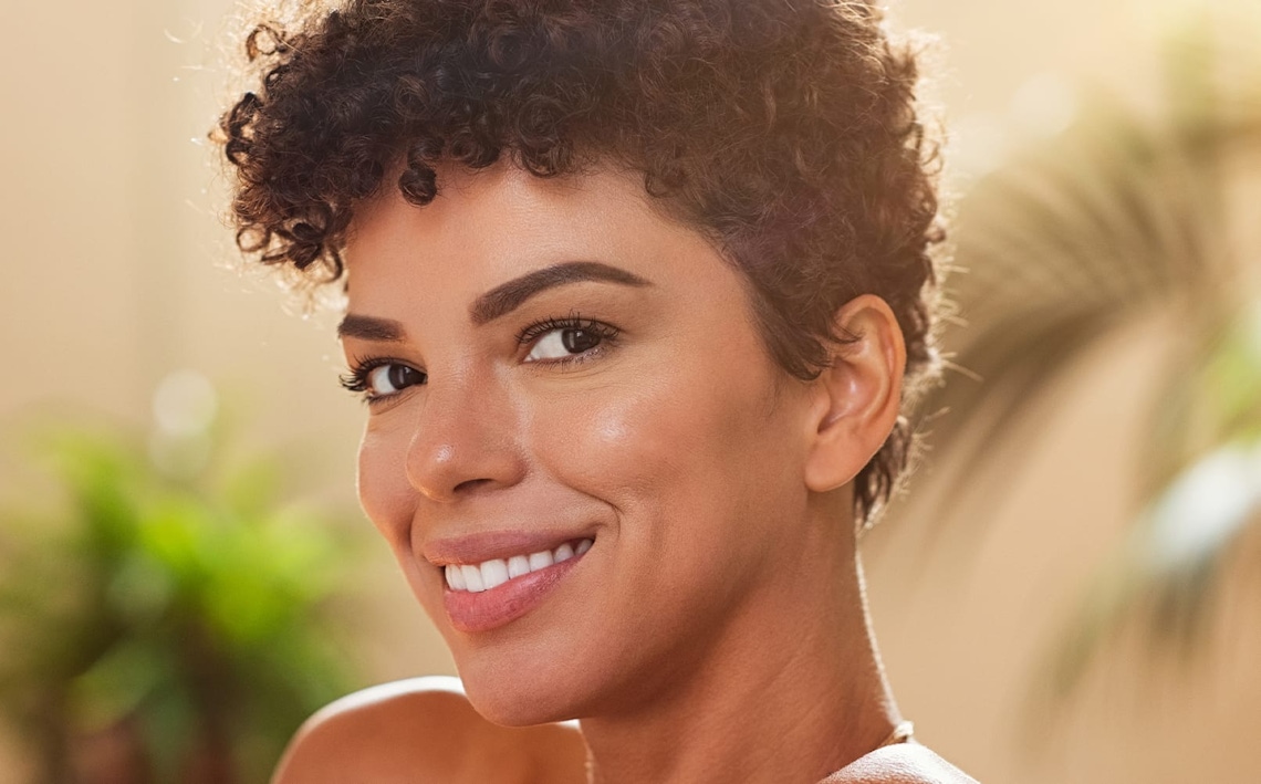 woman with short curly hair smiling forward with plants behind her