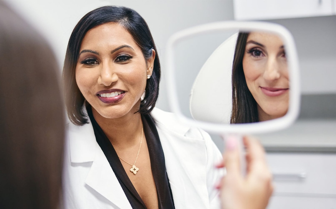 doctor smiling while patient holds a handheld mirror