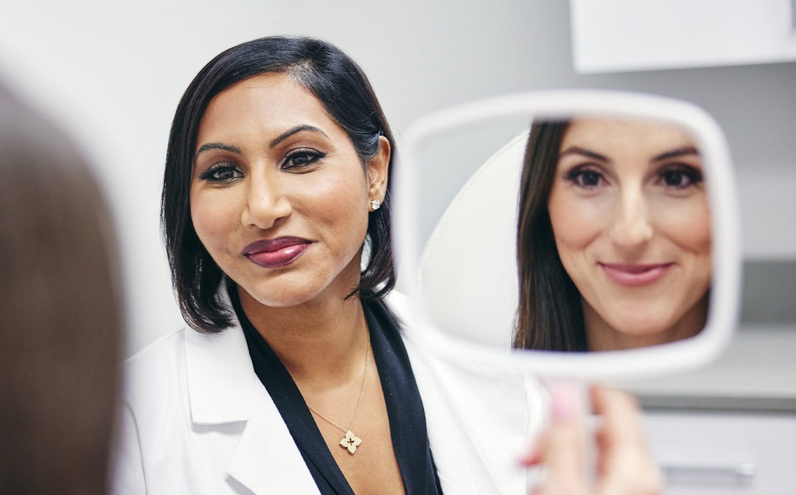 patient looking into handheld mirror while doctor looks at her aswell