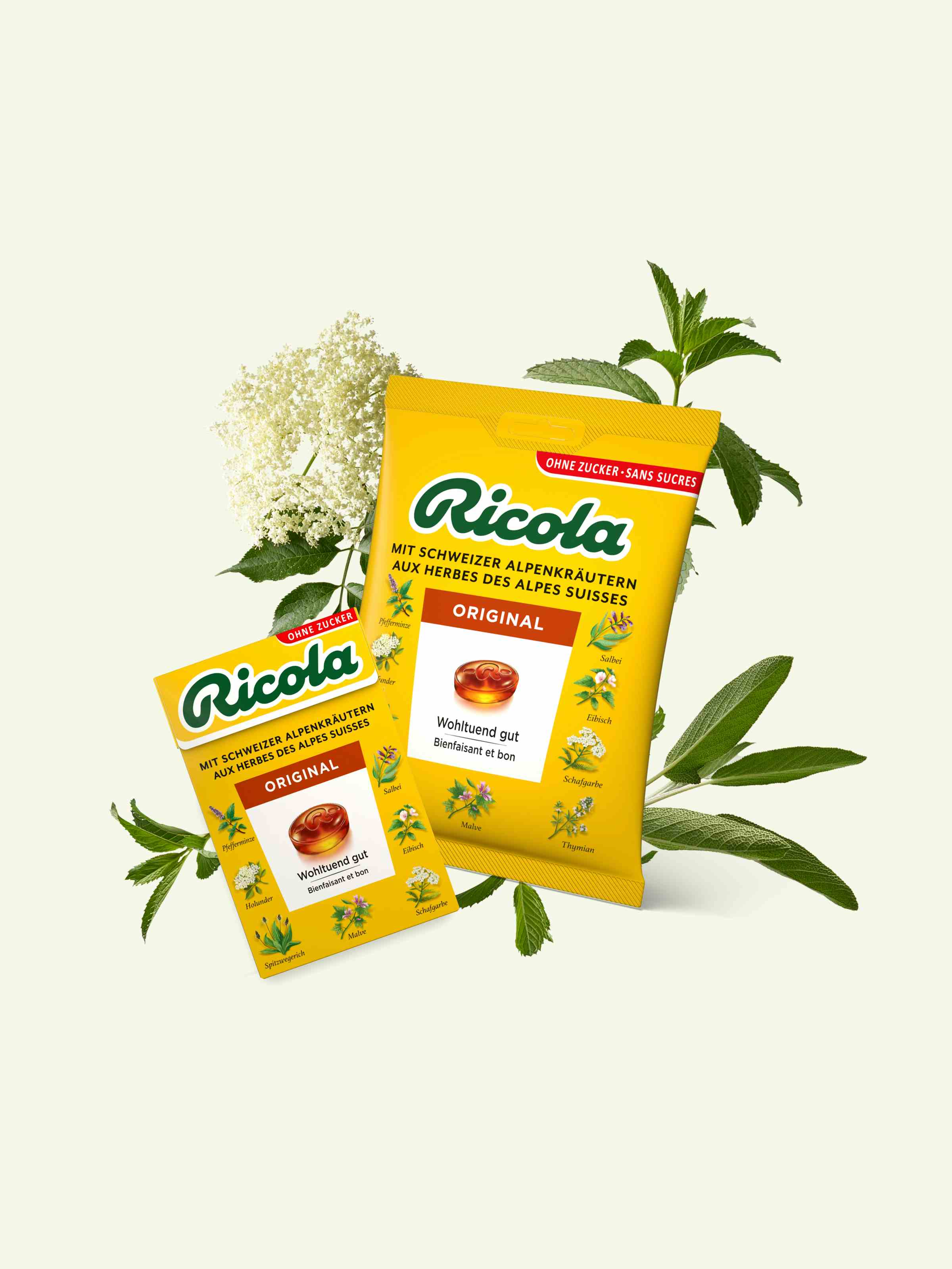 Zwei Packungen Ricola Kräuterbonbons sind inmitten frischer Kräuter ausgestellt. Sie haben eine leuchtend gelbe Verpackung mit mintgrünem Hintergrund.