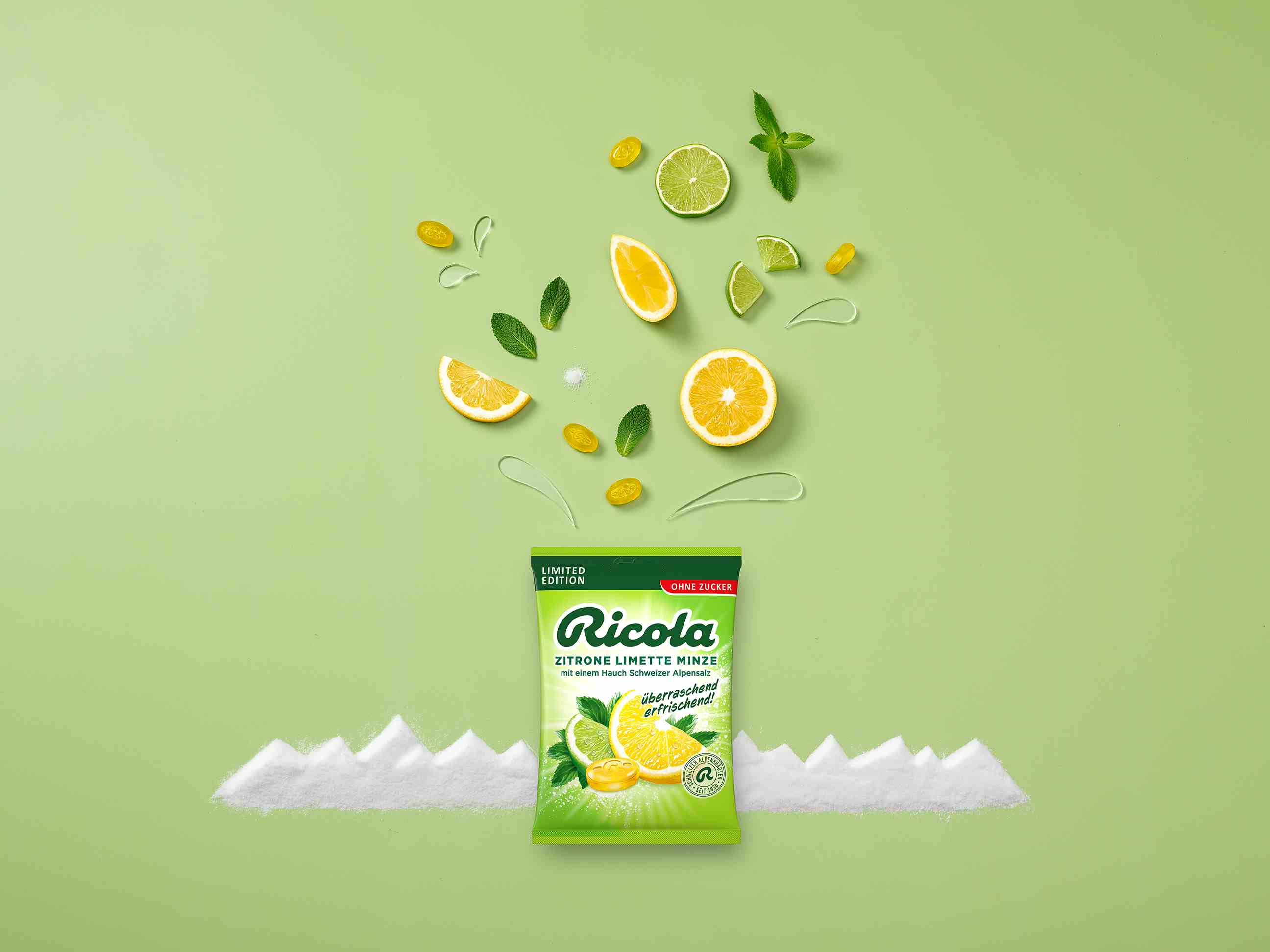Eine Tüte Ricola zuckerfreie Bonbons der Sorte „Zitrone Limette Minze“ steht zentriert auf hellgrünem Hintergrund vor einer stilisierten Gebirgskette aus weißem Salz. Über der Packung schweben Zitronen- und Limettenscheiben, Minzblätter und gelbe Bonbons.