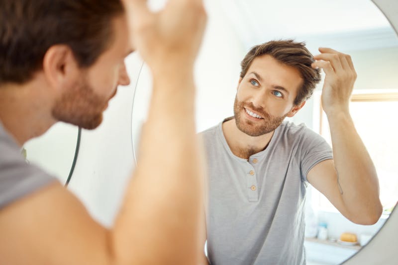 Man examining hair in mirror
