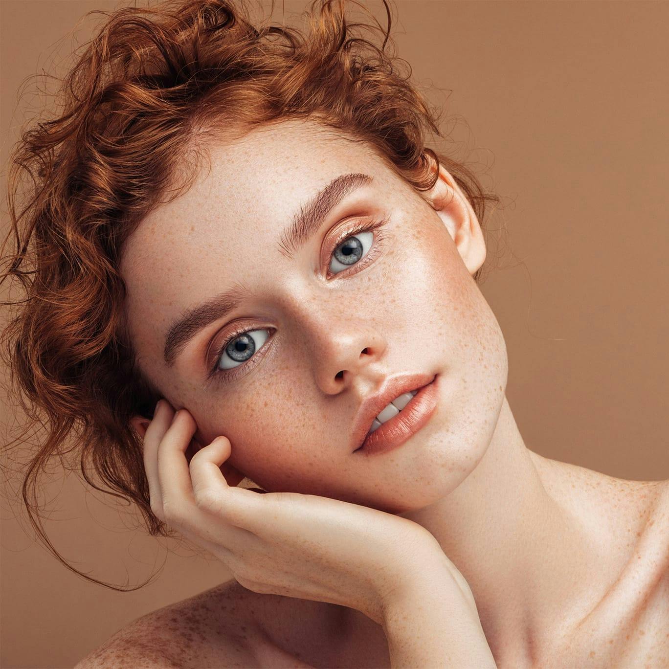 Freckled woman laying cheek on hand