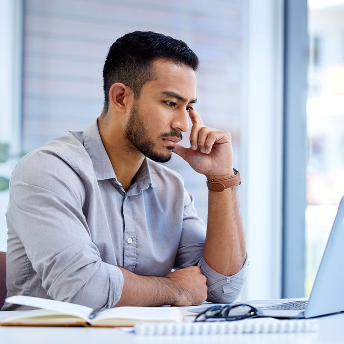 man touching face looking at laptop
