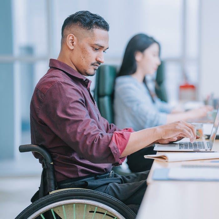 man in wheelchair at desk working on a laptop