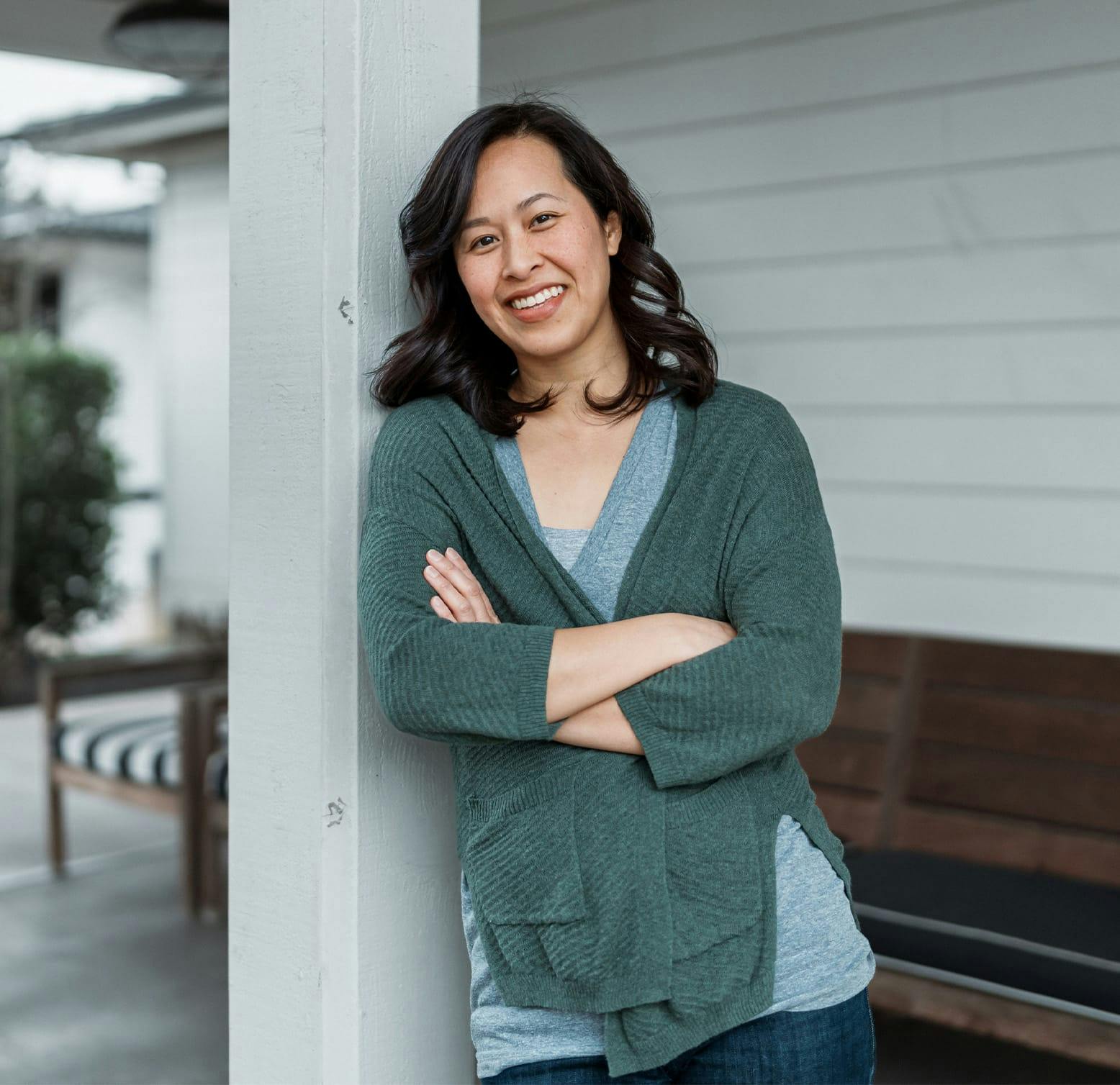 smiling woman leaning against a pole crossing her arms