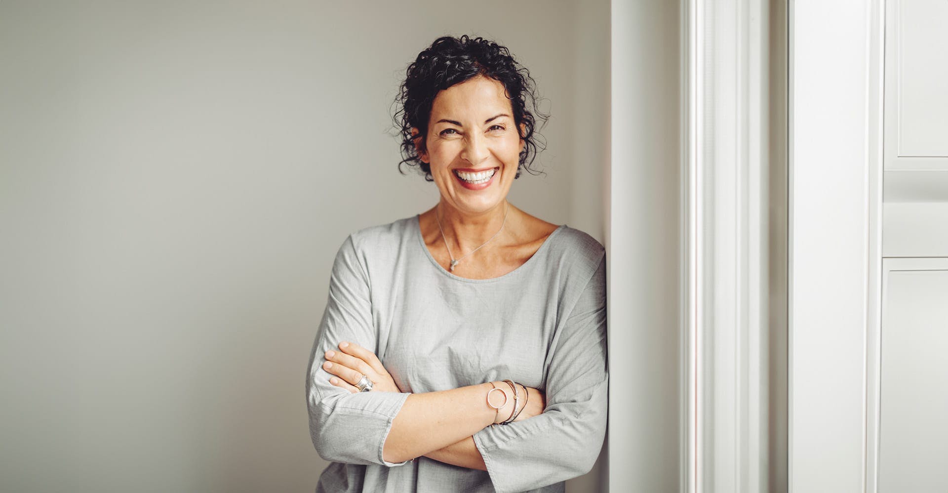 woman smiling while crossing her arms, wearing a grey shirt