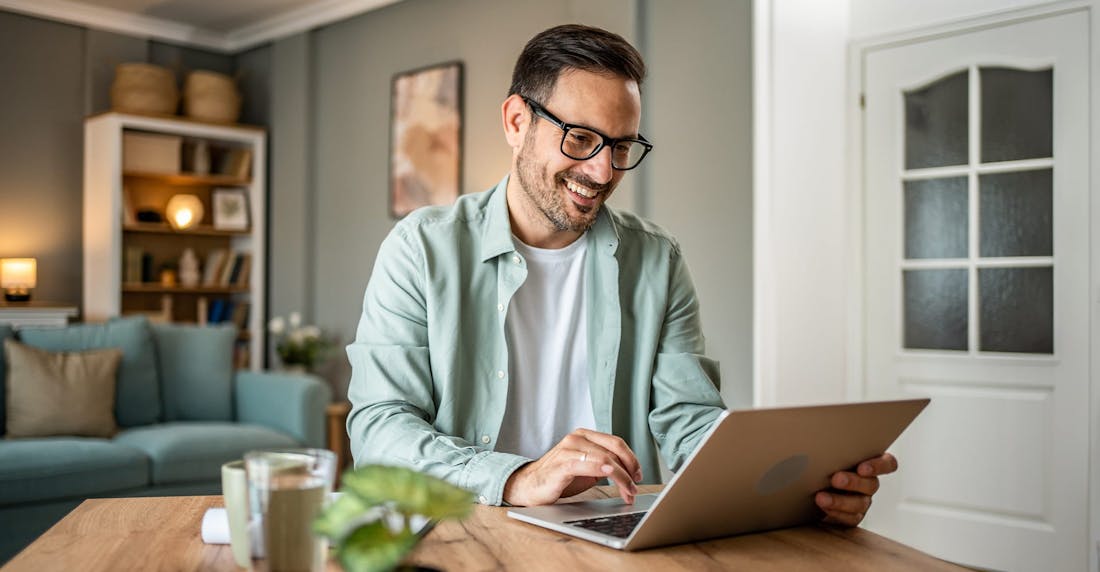 man sitting at a table, typing on a laptop