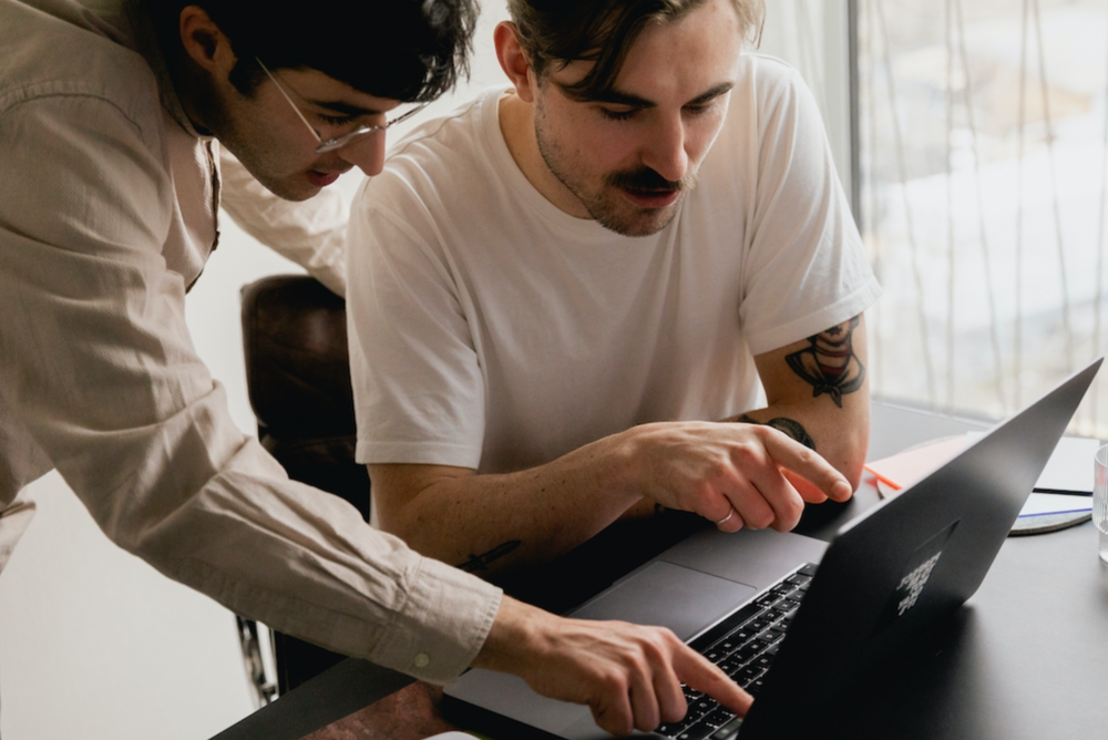 Two young men looking at laptop together while pointing at the screen