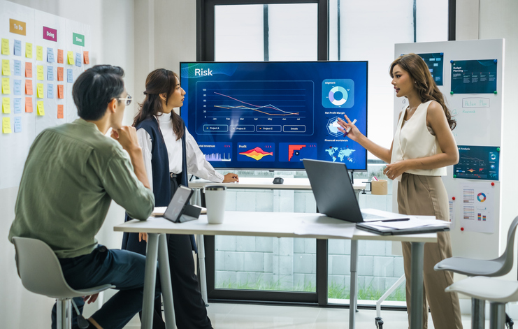 3 people discussing risk, with a screen on the background with various graphs.