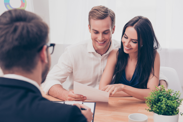 A couple having a look at a home loan document in front of a mortgage broker.