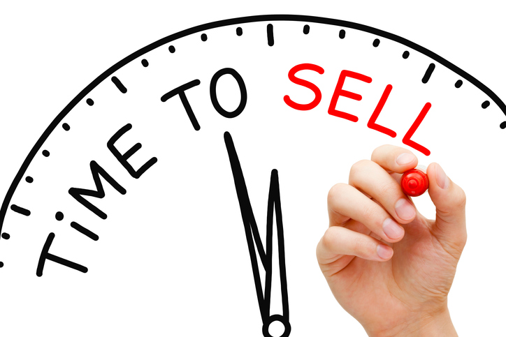 A clock with two hands with writing saying time to sell and a hand holding  a pen