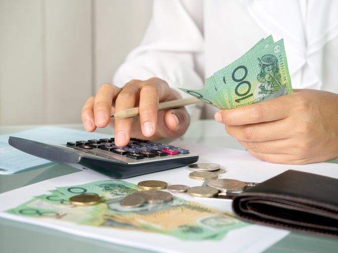 A person holding Australian Dollars with wallet, coins and bills on the side while using the calculator for financial planning.