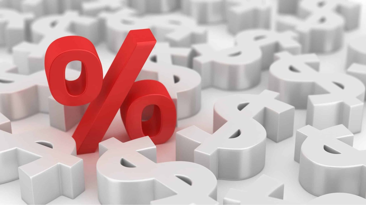 Red Percent sign in the middle of many dollar symbols lying around.