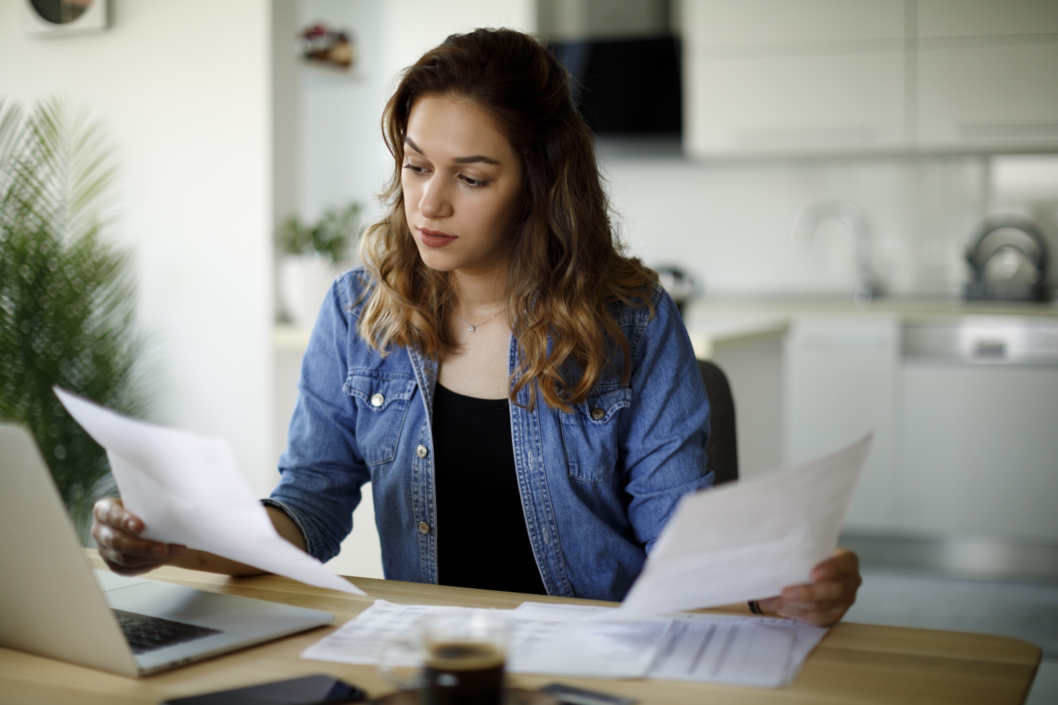 A girl holding 1 paper on her right hand and another paper on the other hand with computer in front of her.