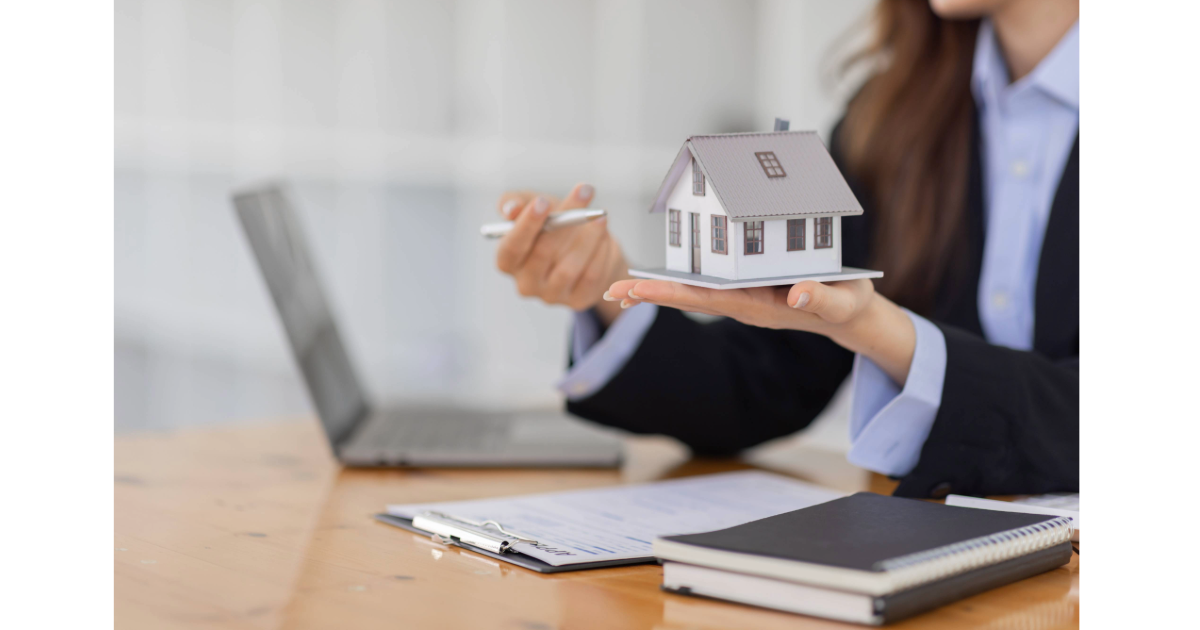 A lady holding a house on her left hand and a pen on her right hand with pen pointing to the house.