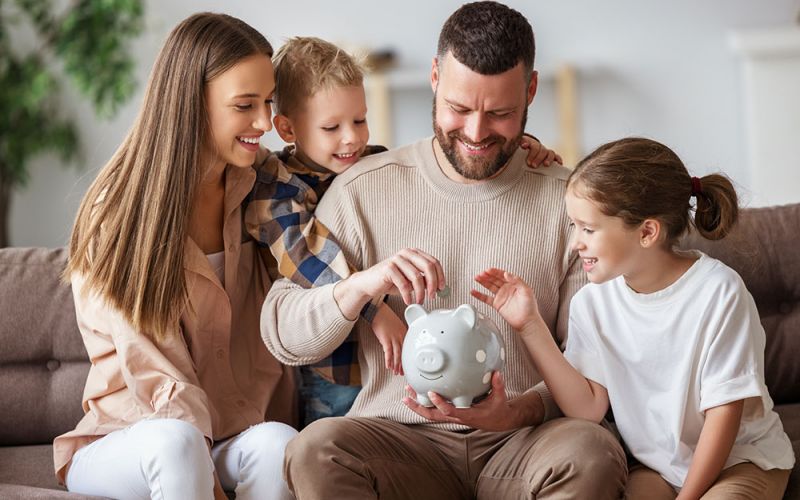 Dad and mum with 2 kids putting coin in a piggy bank.