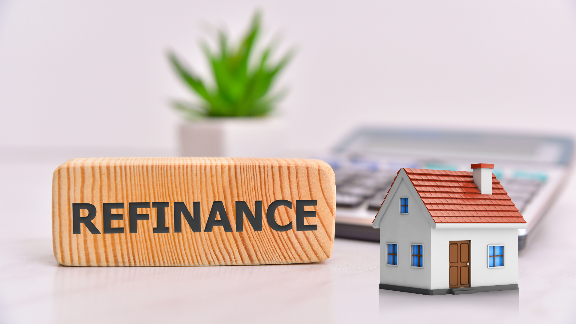The word refinance on a wood with a house beside it and a plant that is blurred at the back.