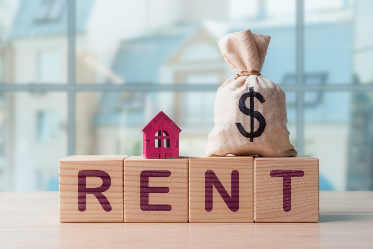 On top of a RENT on wooden blocks are a house and a bag with $ sign.