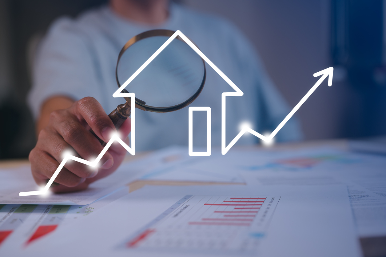 A man holding a magnifying glass pointed to a house with arrows going upward.