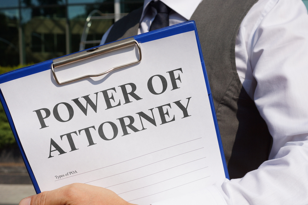 Close-up of a Power of Attorney document on a blue clipboard held by a person in a suit.