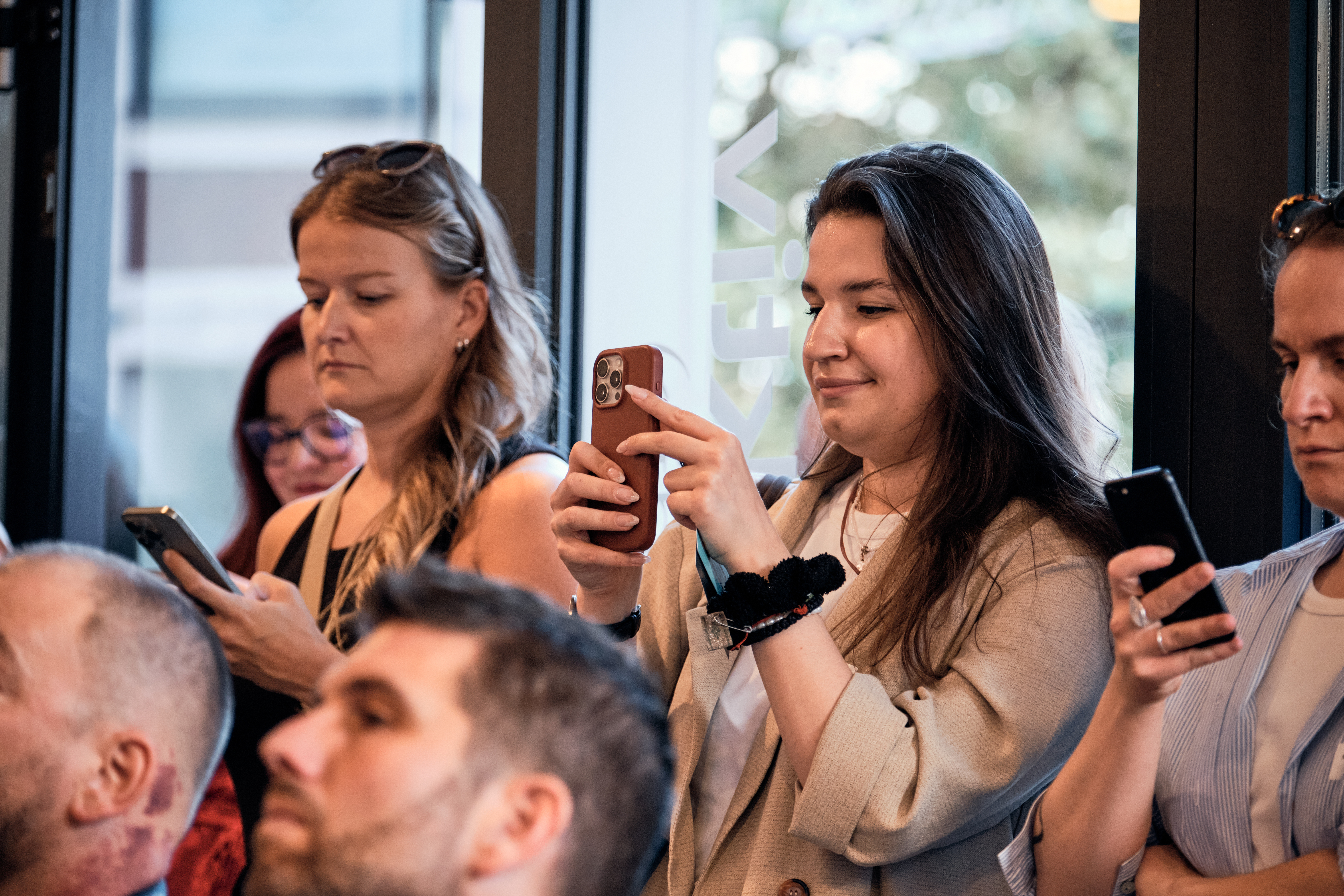 Eine Gruppe von Menschen steht in einem Gebäude und konzentriert sich auf ihre Smartphones. Eine Frau macht mit ihrem Telefon ein Foto oder Video.