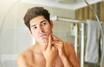 Man popping zit in mirror